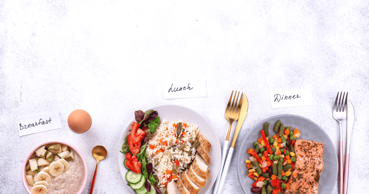 A bowl of oatmeal with bananas labeled “breakfast,” a plate of chicken, rice, and salad labeled “lunch,” and a plate of salmon with mixed vegetables labeled “dinner,” each with matching utensils—beautifully illustrating the principles of Intuitive Eating through balanced and satisfying meals.